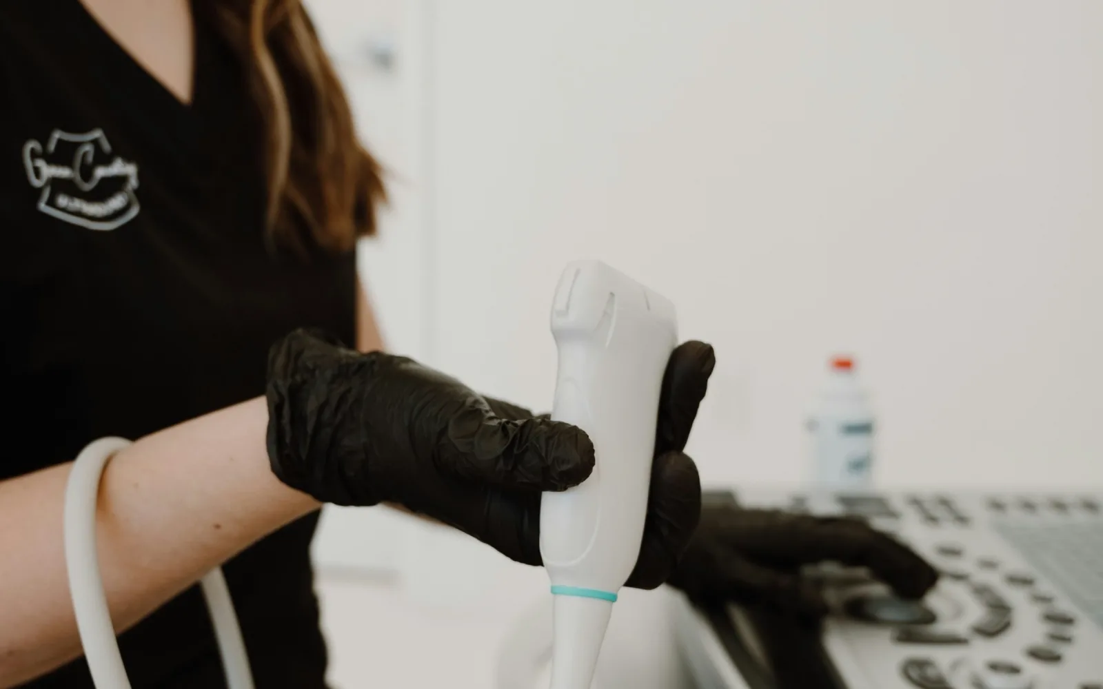 Sonographer holding an ultrasound probe beside the scanner